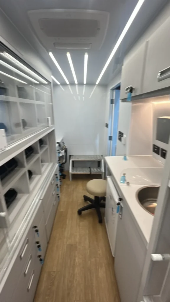Interior da unidade móvel de farmácia com armários de vidro, gavetas com chave, bancada com pia, iluminação LED e ar-condicionado de teto
