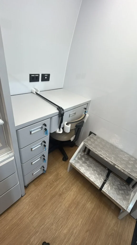 Mesa de atendimento com gaveteiro chaveado, cadeira com fixação e escada de alumínio na farmácia itinerante Eco X